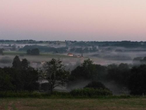 a foggy field with trees and houses in the distance at Gite du jardin du Bout du Ciel in Céron