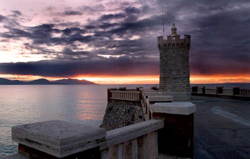 a lighthouse with a bench next to the water at Il Balcone sull'Elba in Piombino