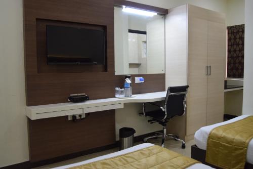a hotel room with a desk and a tv at Thiviyam Airport Hotel in Chennai