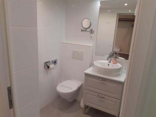 a white bathroom with a toilet and a sink at Hotel Regina in Wengen
