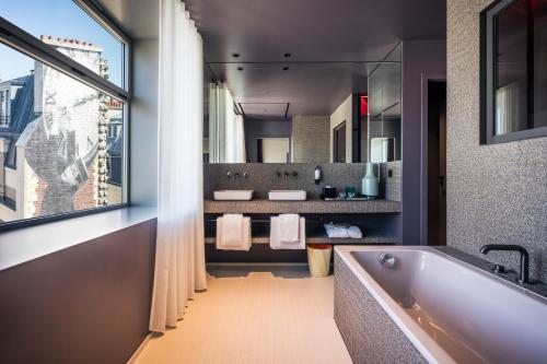 La salle de bains est pourvue d'une baignoire, de 2 lavabos et d'une fenêtre. dans l'établissement Hotel Paradiso, à Paris