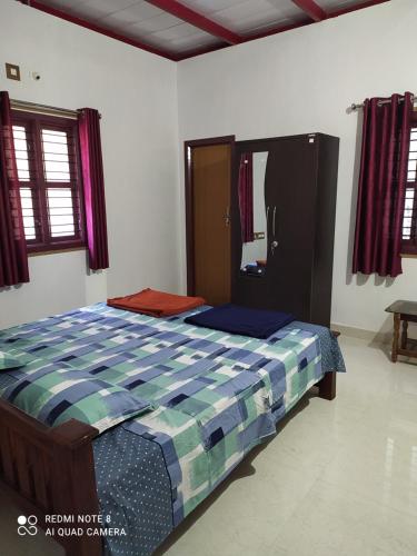 a bedroom with a bed with a blue checked comforter at GARDEN VILLA (Home Stay) in Dharmastala