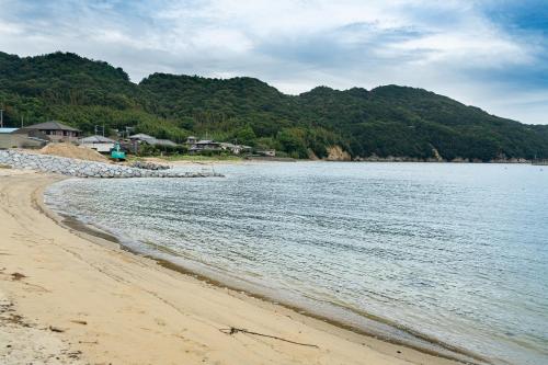 a sandy beach with houses and the water at とまばりゲストハウス in Sanuki