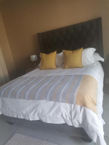 a large bed with white sheets and yellow pillows at Village Kulture - Guest House in Rustenburg