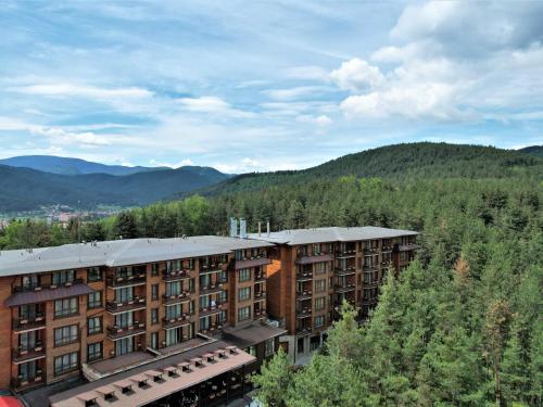 a building in the middle of a forest with mountains at Maxi Park Hotel & Spa in Velingrad