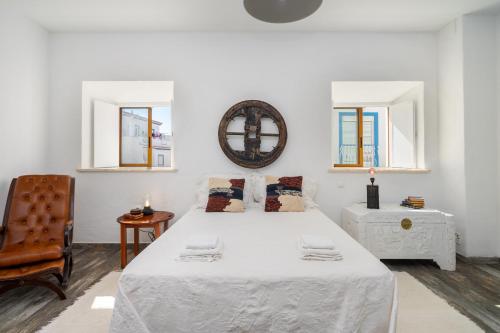 a white bedroom with a large bed and a chair at Casa Celeiro in Estômbar