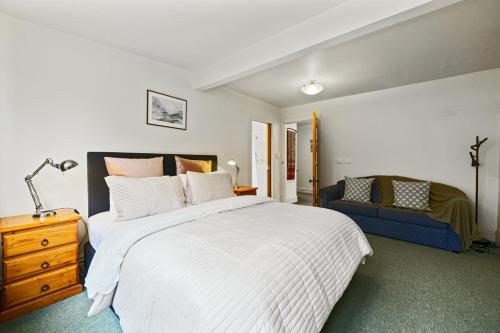 1 dormitorio con 1 cama blanca grande y 1 sofá azul en Pendreigh Cottage - Martinborough Holiday Home en Martinborough 