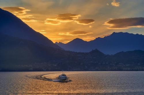 a boat in the water with mountains in the background at The house with red sunsets in Varenna