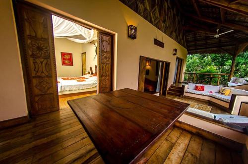 a living room with a wooden table and a bedroom at Le Zahir Lodge in Ambatoloaka