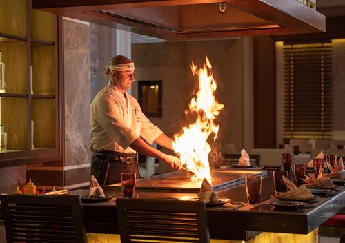 a chef preparing food in a restaurant with flames at Premier Le Reve Hotel & Spa Sahl Hasheesh - Adults Only 16 Years Plus in Hurghada