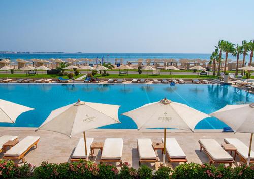 a large swimming pool with umbrellas and chairs and the ocean at Premier Le Reve Hotel & Spa Sahl Hasheesh - Adults Only 16 Years Plus in Hurghada