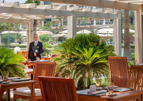 a man in a suit standing in a restaurant with tables at Premier Le Reve Hotel & Spa Sahl Hasheesh - Adults Only 16 Years Plus in Hurghada