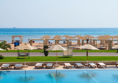 a pool with chairs and umbrellas next to the beach at Premier Le Reve Hotel & Spa Sahl Hasheesh - Adults Only 16 Years Plus in Hurghada