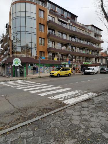 a yellow car driving down a street with a building at Апартамент - студио в кв Сарафово с морски изглед in Burgas City