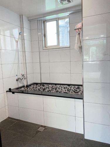 a white tiled bathroom with a tub and a window at 溫沙堡汽車旅館 Windsor Castle Garden Motel in Jiaoxi