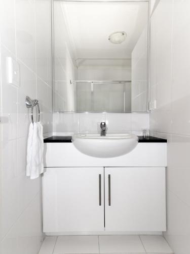 a white bathroom with a sink and a mirror at Horizon Holiday Apartments in Narooma