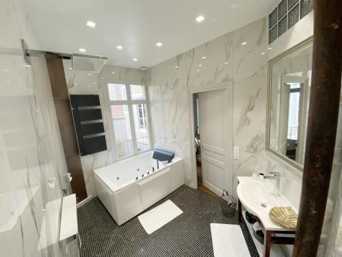 a white bathroom with a tub and a sink at Le Clovis Suites Spa Sauna in Reims