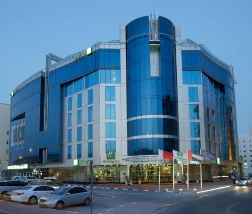 un gran edificio de cristal con coches estacionados frente a él en Holiday Inn Dubai Al Barsha, an IHG Hotel, en Dubái