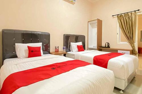 two beds in a room with red and white at RedDoorz Plus at Permata Gueshouse Lampung in Lampung