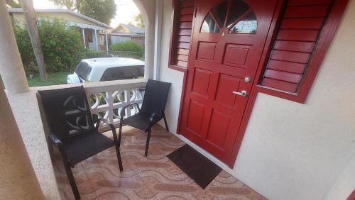 a red door and two chairs on a porch at Carmen's Cozy Studio in Bridgetown