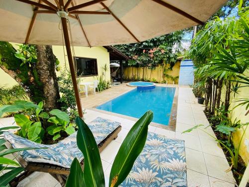 uma piscina com um guarda-sol e duas cadeiras e uma mesa em ILHABEACH GUESTHOUSE em Ilhabela
