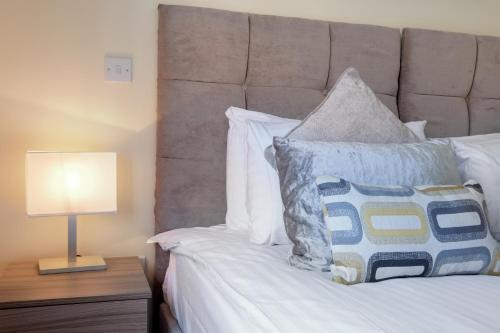 a bed with white pillows and a lamp on a table at London Heathrow Living Holywell Serviced Houses - 3 and 4 bedrooms By Ferndale in Stanwell