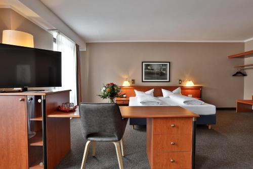 バーデン・バーデンにあるHotel Quellenhofのベッド、デスク、テレビが備わるホテルルームです。