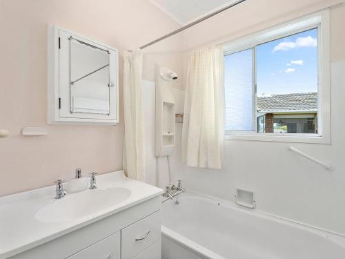ein weißes Bad mit einem Waschbecken und einem Fenster in der Unterkunft Central Riverside Retreat - Taupo Holiday Home in Taupo