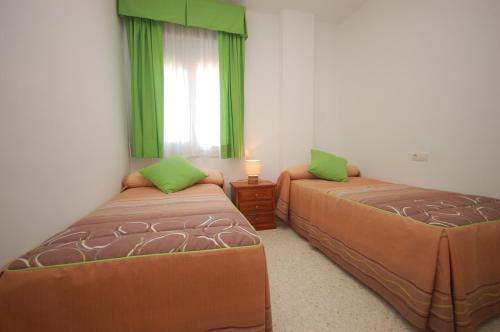 1 dormitorio con 2 camas y una ventana con cortinas verdes en Holi-Rent Albatros, en Sanlúcar de Barrameda