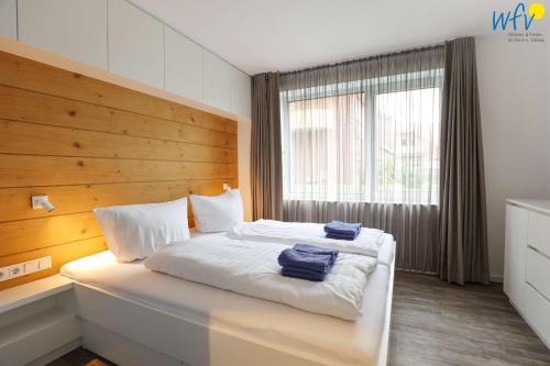 a bedroom with a white bed with a wooden headboard at Haus Talita - Wohnung DELTA in Juist