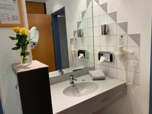 a bathroom with a sink and a vase of flowers at Hotel am Stadtpark in Borken