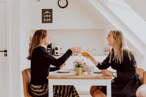 Duas mulheres sentadas à mesa a beber sumo de laranja. em Ramslo em Herselt