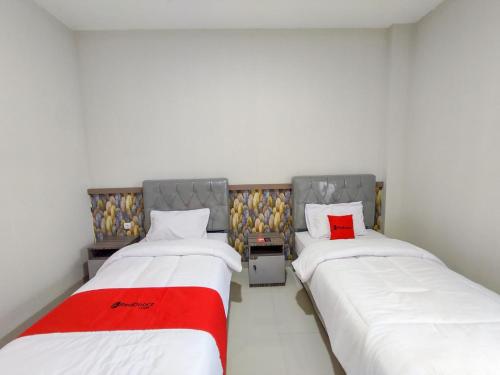 two beds in a room with a red blanket between them at RedDoorz Syariah near GOR Satria Area in Purwokerto