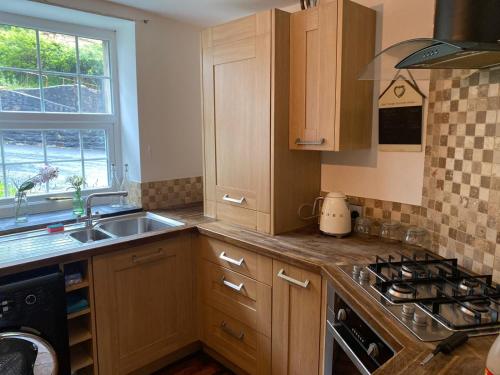 a kitchen with wooden cabinets and a sink and a stove at 2-Bed Cottage in in Welsh Valley Nr Swansea in Swansea