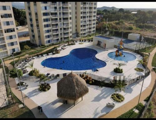 a large swimming pool with a straw umbrella and buildings at Lindo apartamento cerca a Girardot in Ricaurte