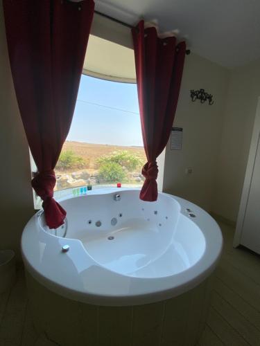 a bath tub with a window with red curtains at אלרון - אירוח בגולן in Ani'am