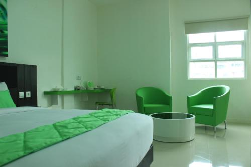 a bedroom with a bed and two green chairs at Evan Hotel Jambi in Jambi