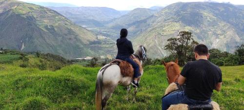 two people riding horses in a field with mountains at Hotel y Spa Isla de Baños in Baños