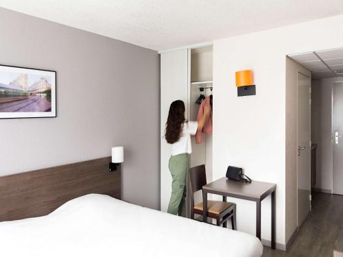 una mujer de pie en una habitación de hotel mirando en un armario en Aparthotel Adagio Access Orléans en Orléans