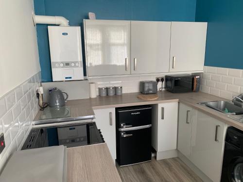 a kitchen with white cabinets and a black refrigerator at The Cochno Flat, Clydebank in Dalmuir