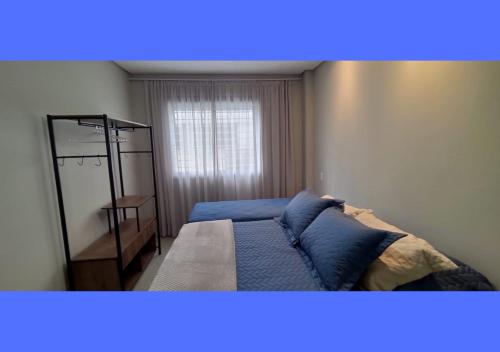 ein Schlafzimmer mit einem Bett mit blauen Kissen und einem Fenster in der Unterkunft Apartamento Garden em Palmas do Arvoredo SC in Governador Celso Ramos