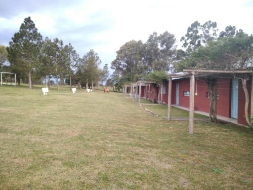 a large grass field with a red building and trees at Estancia turistica la Providencia in Termas del Daymán