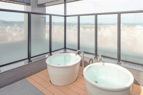 un bagno con vasca in una camera con finestre di HOTEL AMANEK Asahikawa a Asahikawa