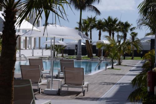 a row of chairs and an umbrella next to a swimming pool at Island Home Fuerteventura in Corralejo