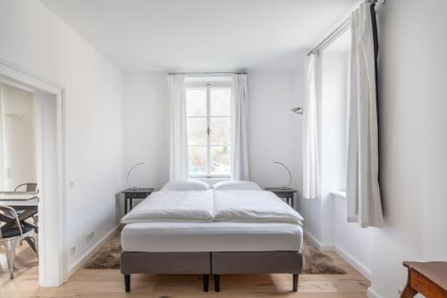 a white bedroom with a bed and two windows at Villa Bertholini in Bad Ischl