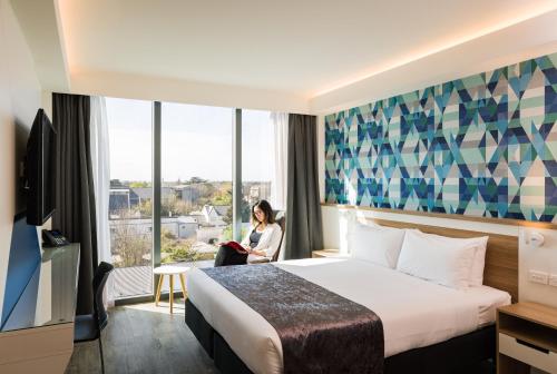 a woman sitting in a hotel room with a bed and a window at Carnmore Hotel Christchurch in Christchurch