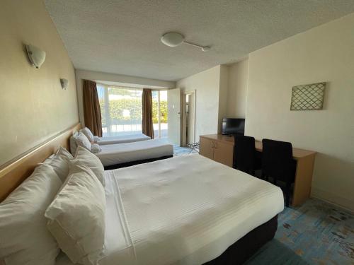 a bedroom with two beds and a desk and a window at Haven Marina Motel in Adelaide