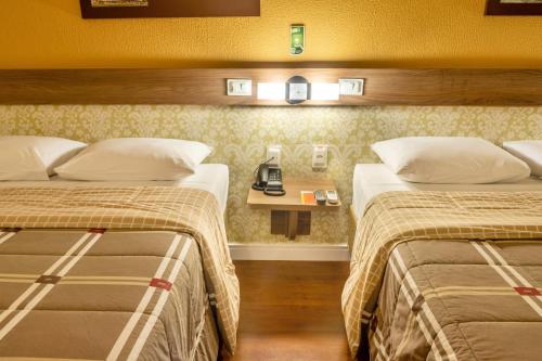 a hotel room with two beds and a phone on a table at Hotel 10 São Leopoldo in São Leopoldo