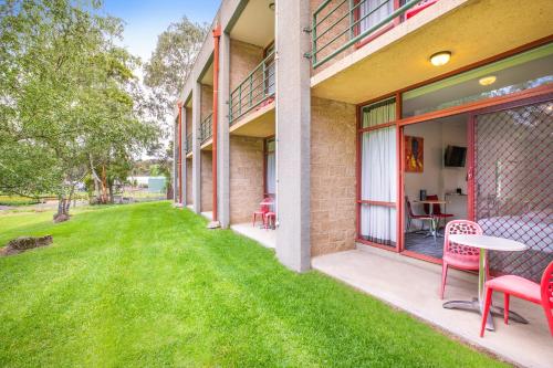 a patio with red chairs and a table on a lawn at Nightcap at York on Lilydale in Mount Evelyn