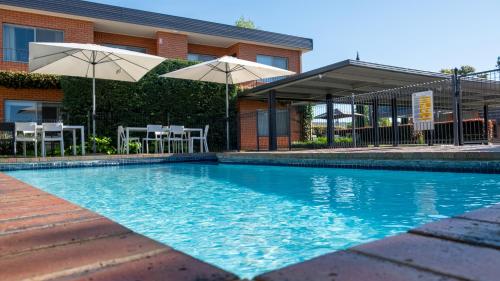 uma piscina com dois guarda-sóis e um edifício em Parkview Motor Inn and Apartments em Wangaratta